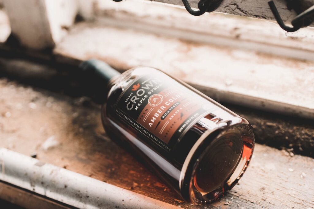 Close-up of amber maple syrup bottle lying on rustic windowsill in natural light.